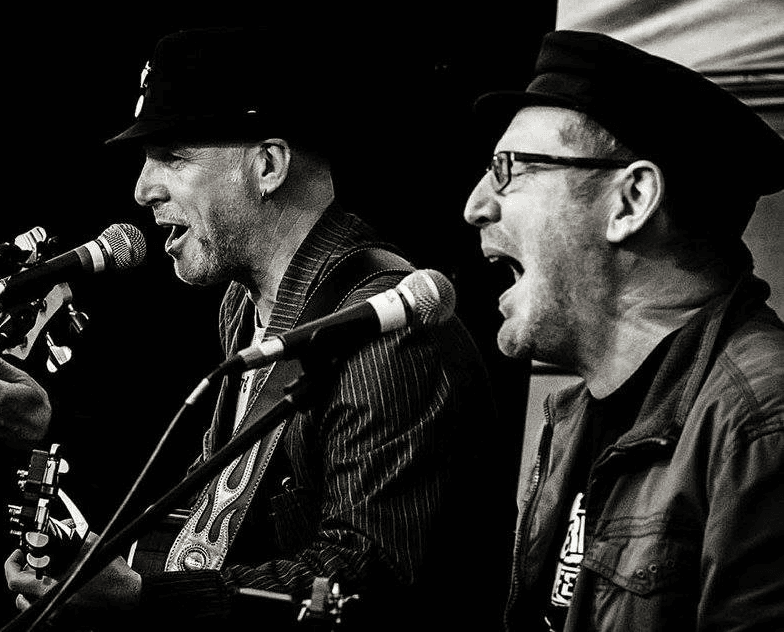Les Glover and Henry Priestman onstage playing guitar in black and white